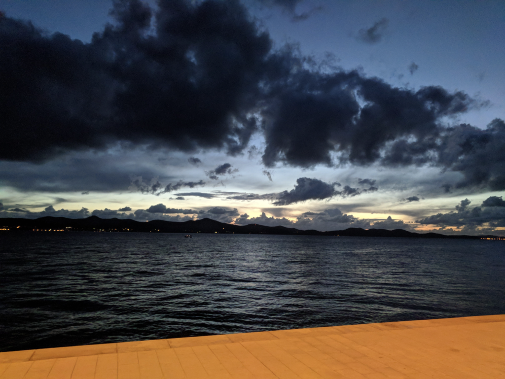 Adriatic Sea at dusk from the Zadar Croatia waterfront promenade, storm clouds over distant mountains