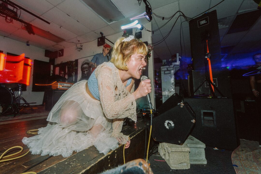 Woman on a stage screaming into a microphone.